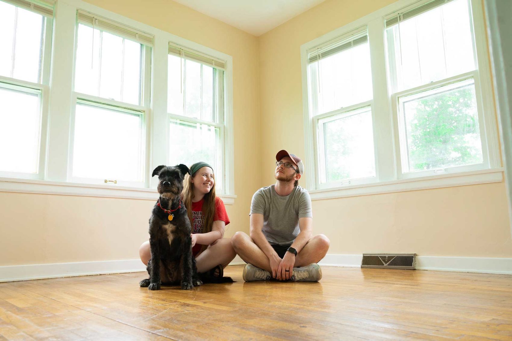 Young couple with a large dog sitting on a hardwood floor in an empty room