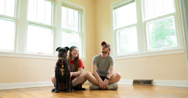 Young couple with a large dog sitting on a hardwood floor in an empty room