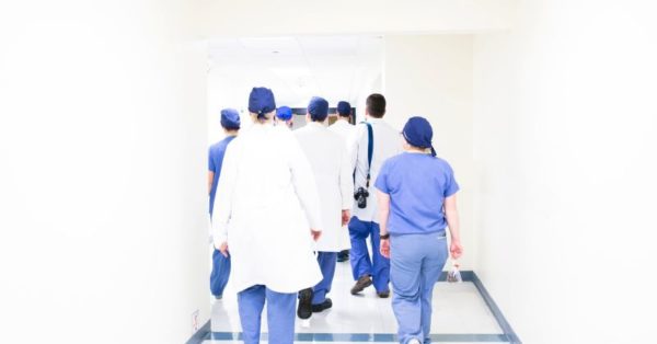 Large group of nurses and doctors walking down a bright hallway in blue scrubs and white lab coats