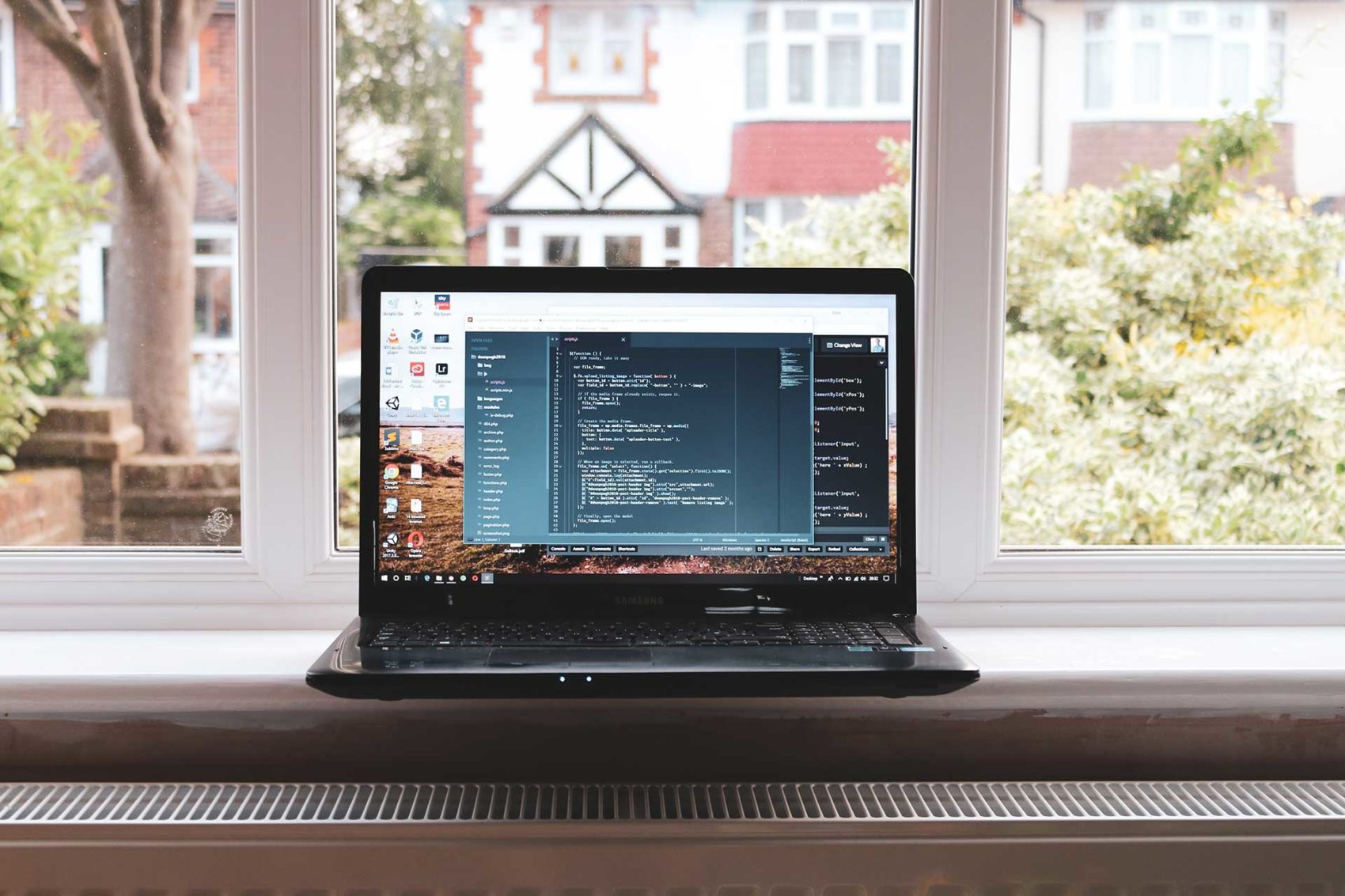 Open laptop displaying a coding program sitting on a window sill