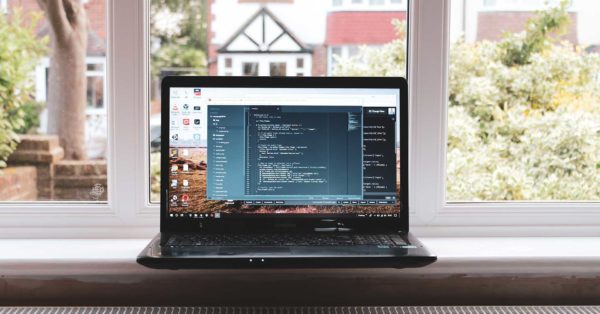 Open laptop displaying a coding program sitting on a window sill