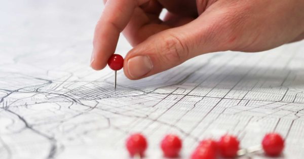 Closeup of a person's hand placing a red pin into a map